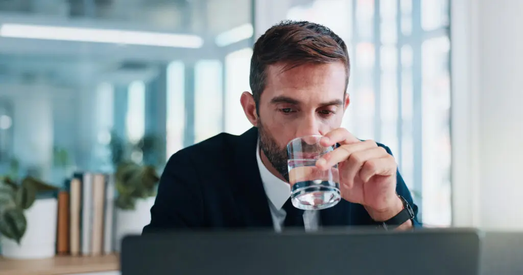 Businessman, water or laptop with thirst at office desk for hydration or refreshing drink. Man, employee or mineral liquid at computer for natural sustainability, relief or healthy wellness at work.