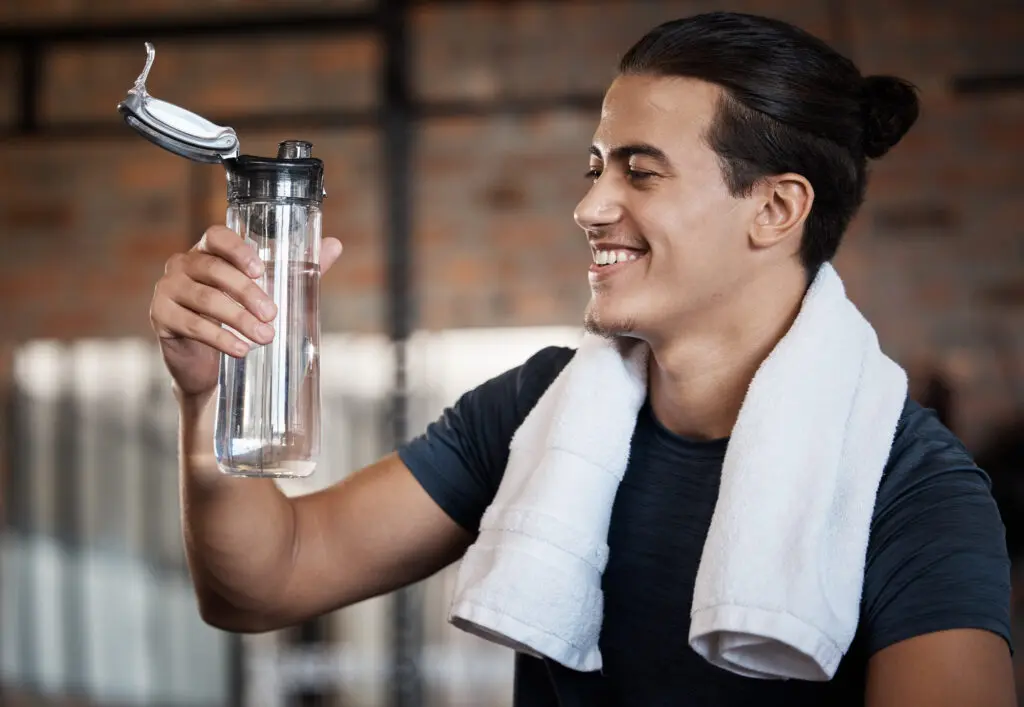 Fitness, smile and drinking water with man in gym for health, exercise and cardio endurance. Wellness, weightlifting or training with body builder on break in sports center for stamina, detox or diet.