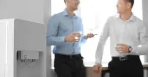 A man holding a clear cup underneath a stream of water that's coming out of the cold side of a water dispenser.