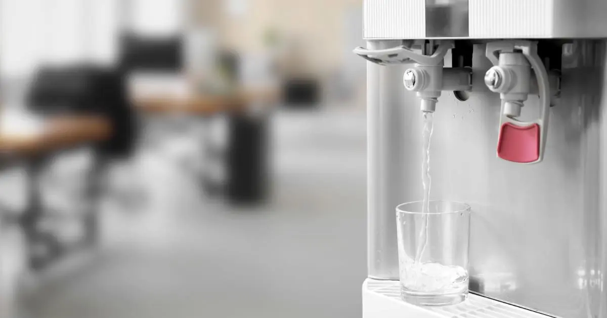 Fresh water pouring from a modern office cooler into a clear glass with a close-up view of the hot and cold dispensers.